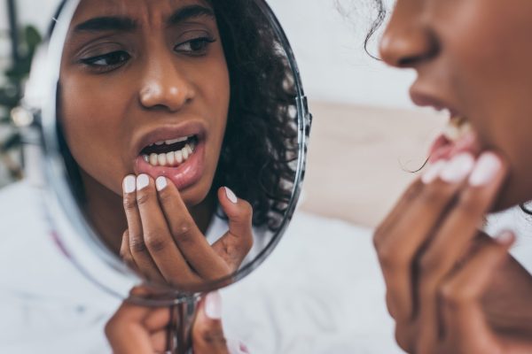 Young woman with painful gums looking in a handheld mirror