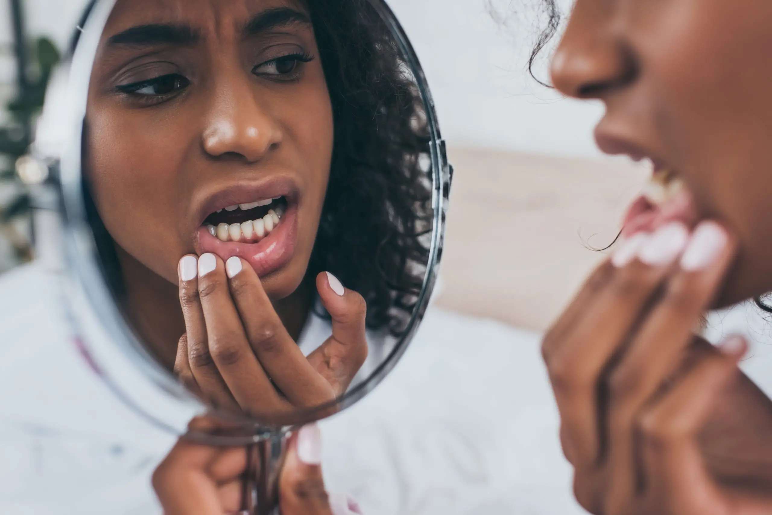 Young woman with painful gums looking in a handheld mirror